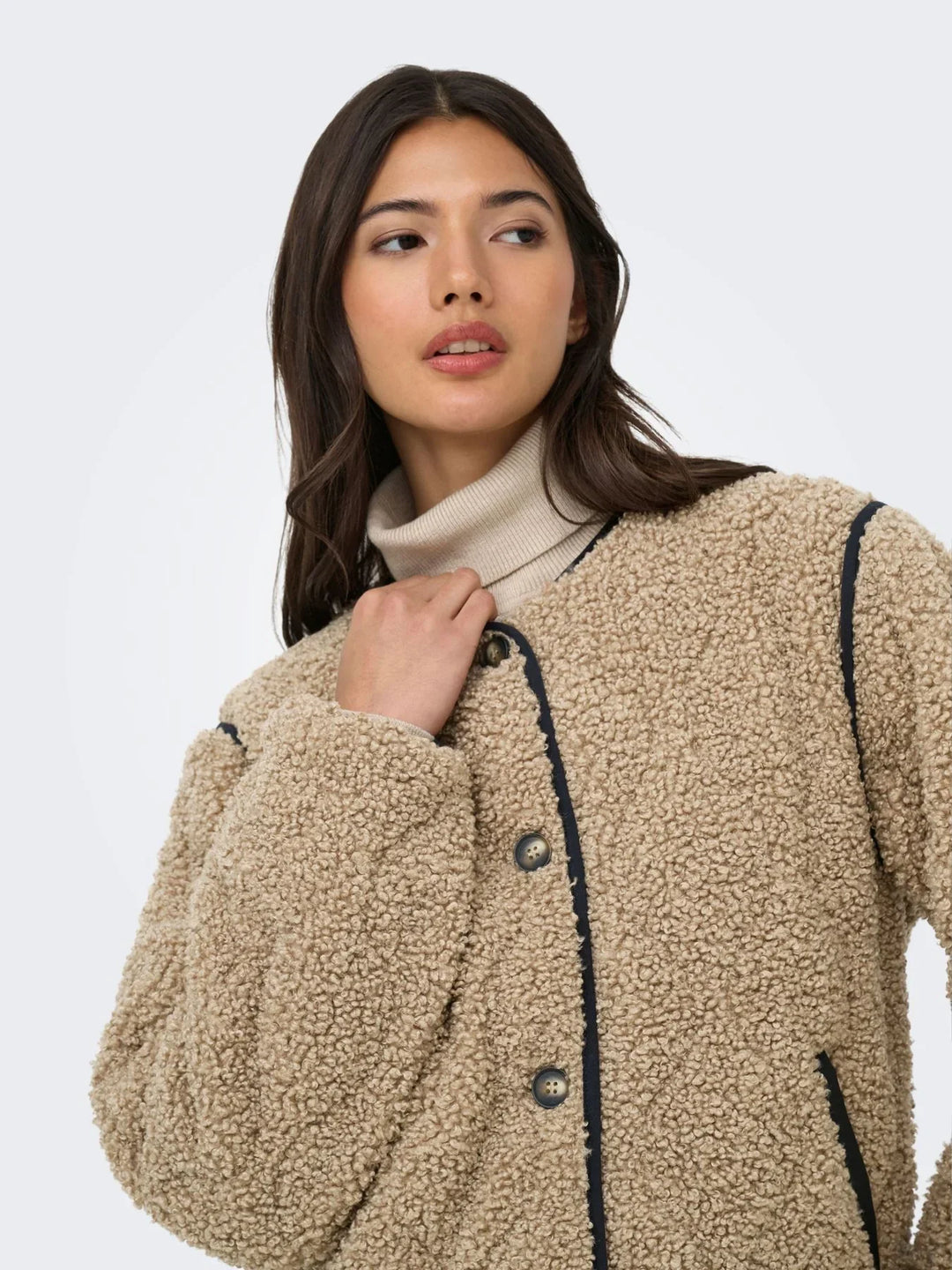 Model trägt eine beige Teddyjacke mit dunklen Kontrastdetails über einem hellen Rollkragenpullover. Die Nahaufnahme betont die weiche, strukturierte Oberfläche und den gemütlichen Herbst-Look.
