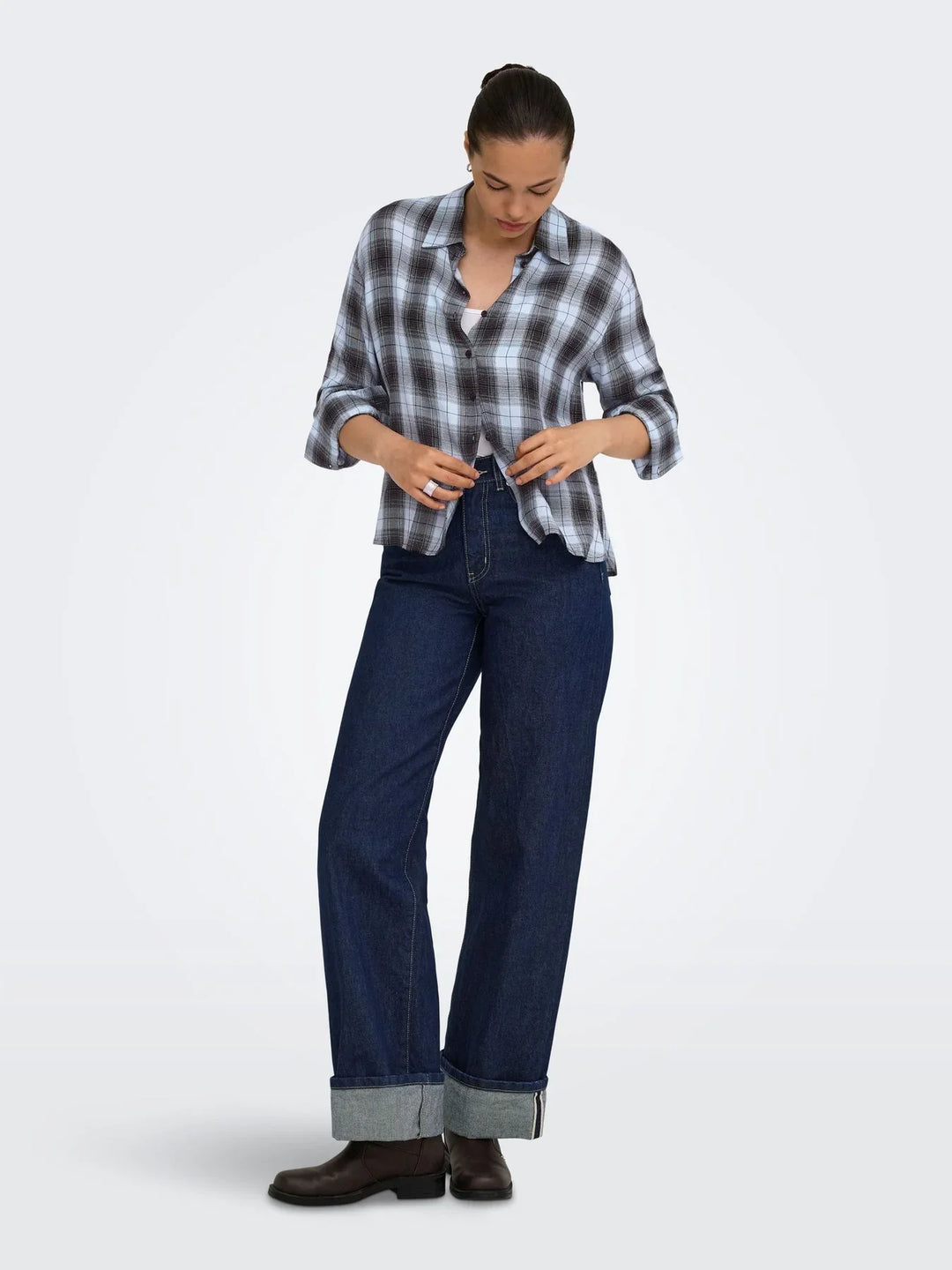 Model trägt eine blau-grau karierte Bluse zu einer dunkelblauen Wide-Leg-Jeans mit breitem Umschlag. Braune Stiefeletten ergänzen den lässigen Herbst-Look.