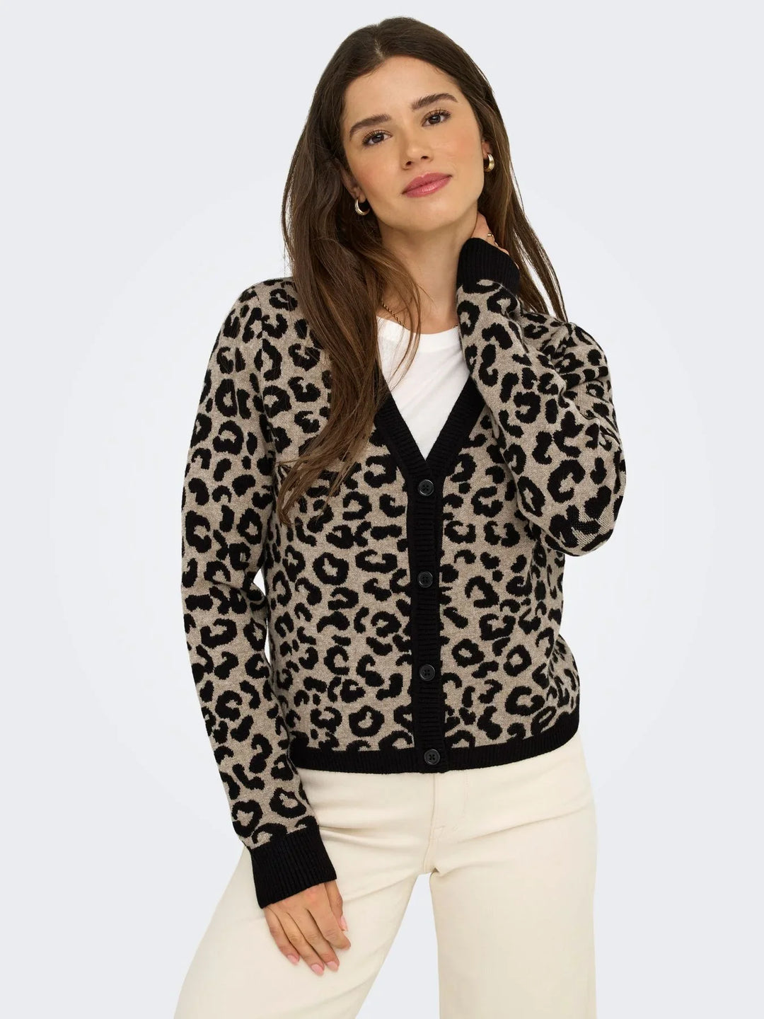 Model trägt eine beige-schwarze Strickjacke mit auffälligem Leo-Muster und Knopfleiste über einem weißen Oberteil. Die helle Hose ergänzt den modernen Leo-Look.