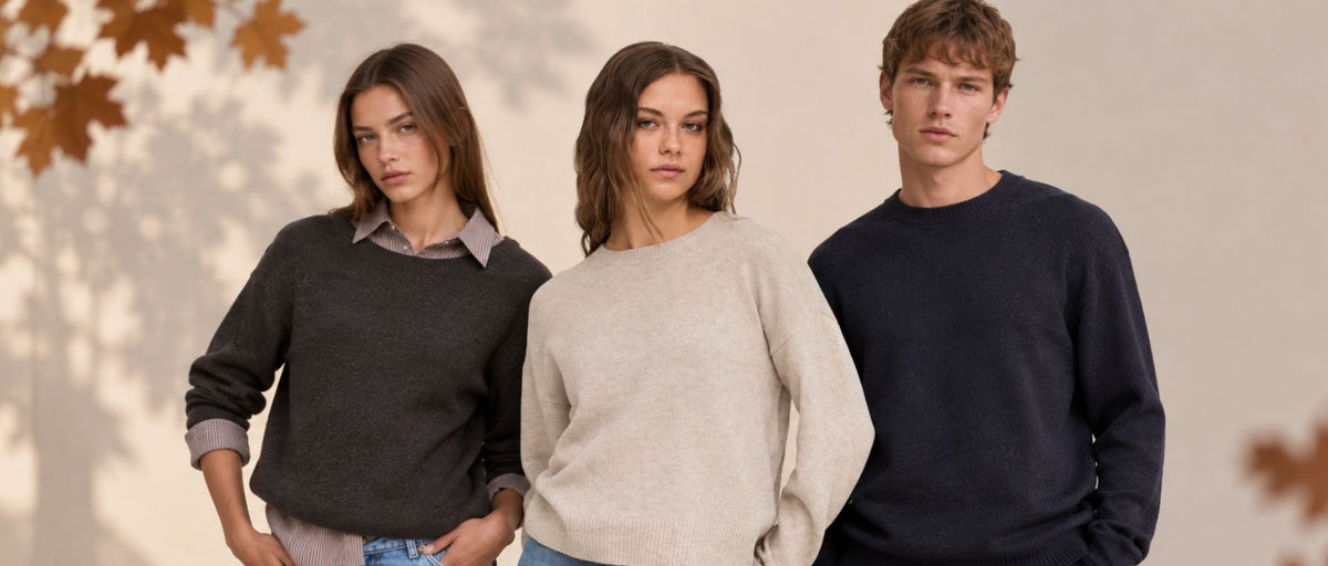 Drei Models präsentieren herbstliche Damen- und Herrenmode vor einem warmen, minimalistischen Hintergrund mit Herbstblättern. Zu sehen sind verschiedene Strick-Looks in Creme, Dunkelbraun und Dunkelblau.