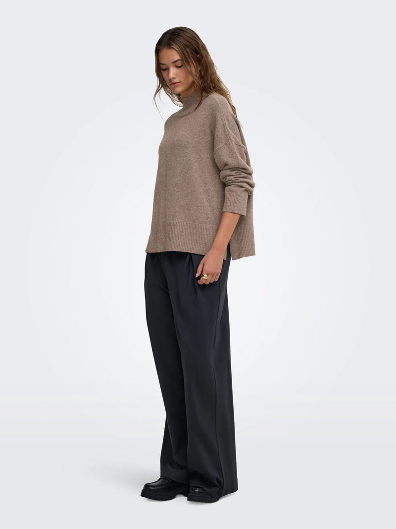 Model trägt einen taupefarbenen Strickpullover mit Stehkragen und lockerer Passform zu einer schwarzen Wide-Leg-Hose. Der schlichte Look wirkt modern, zeitlos und herbstlich.