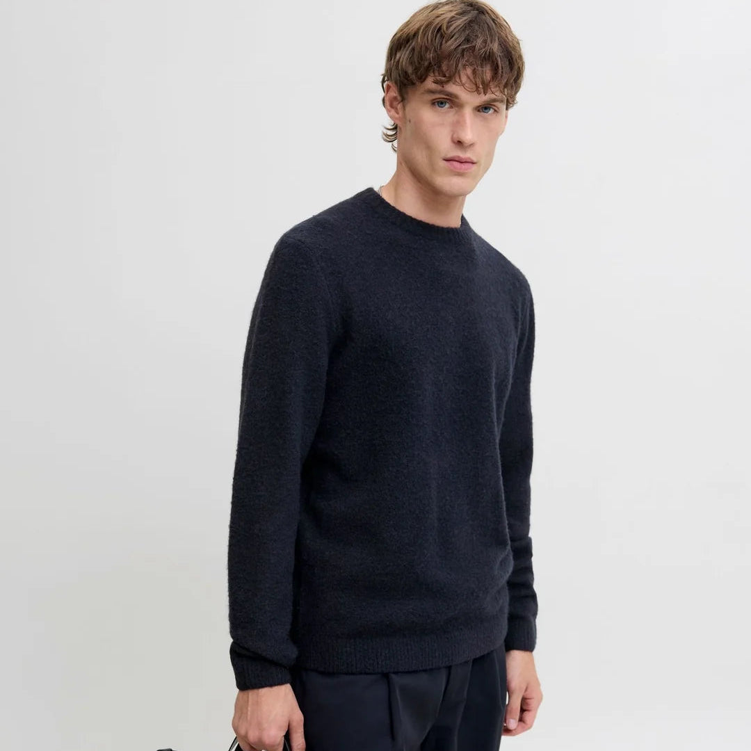 Herren-Strickpullover in Dunkelblau mit Rundhalsausschnitt, modern kombiniert mit dunkler Hose und schwarzer Tasche.